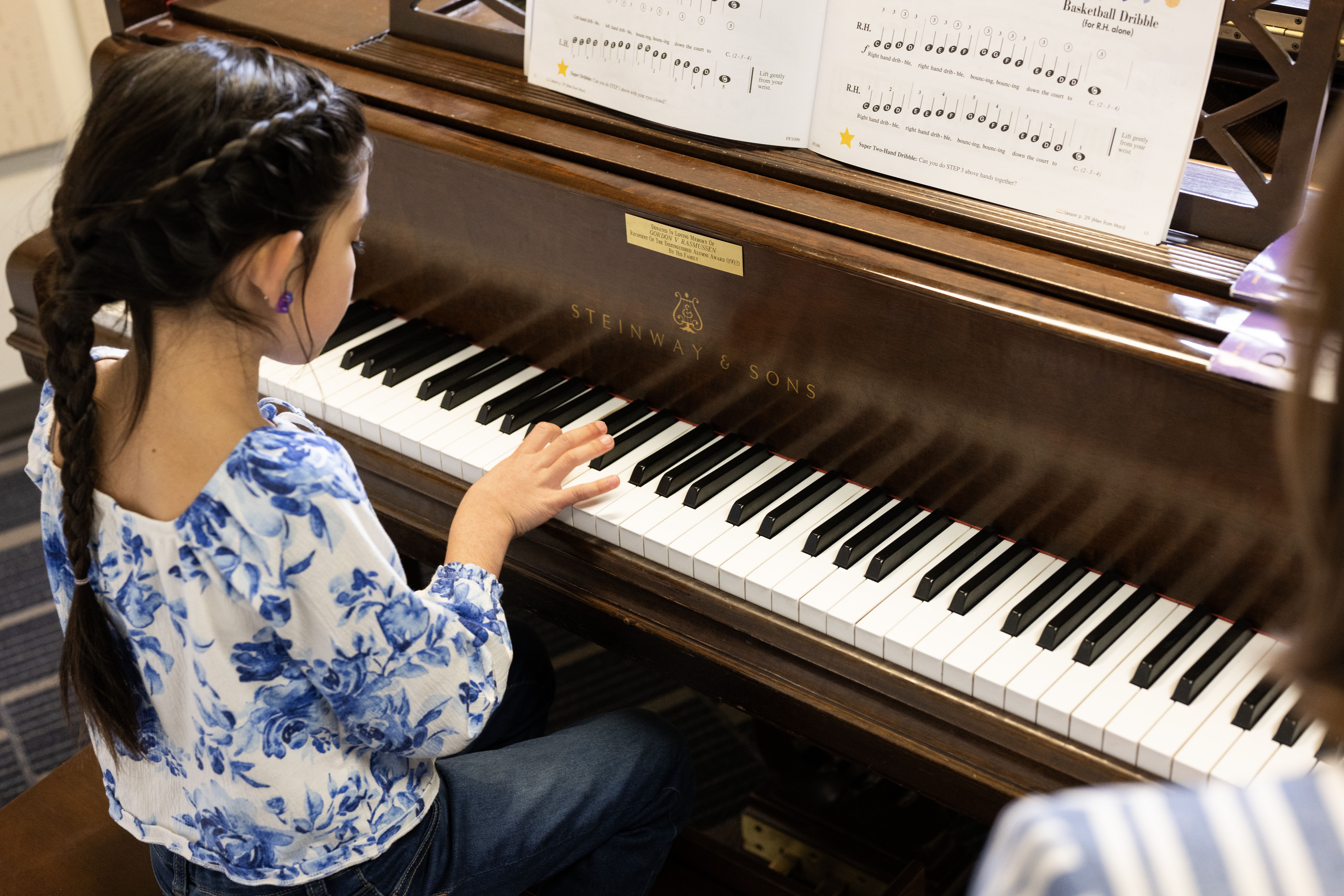 An instructor sitting at a piano watching her student play.