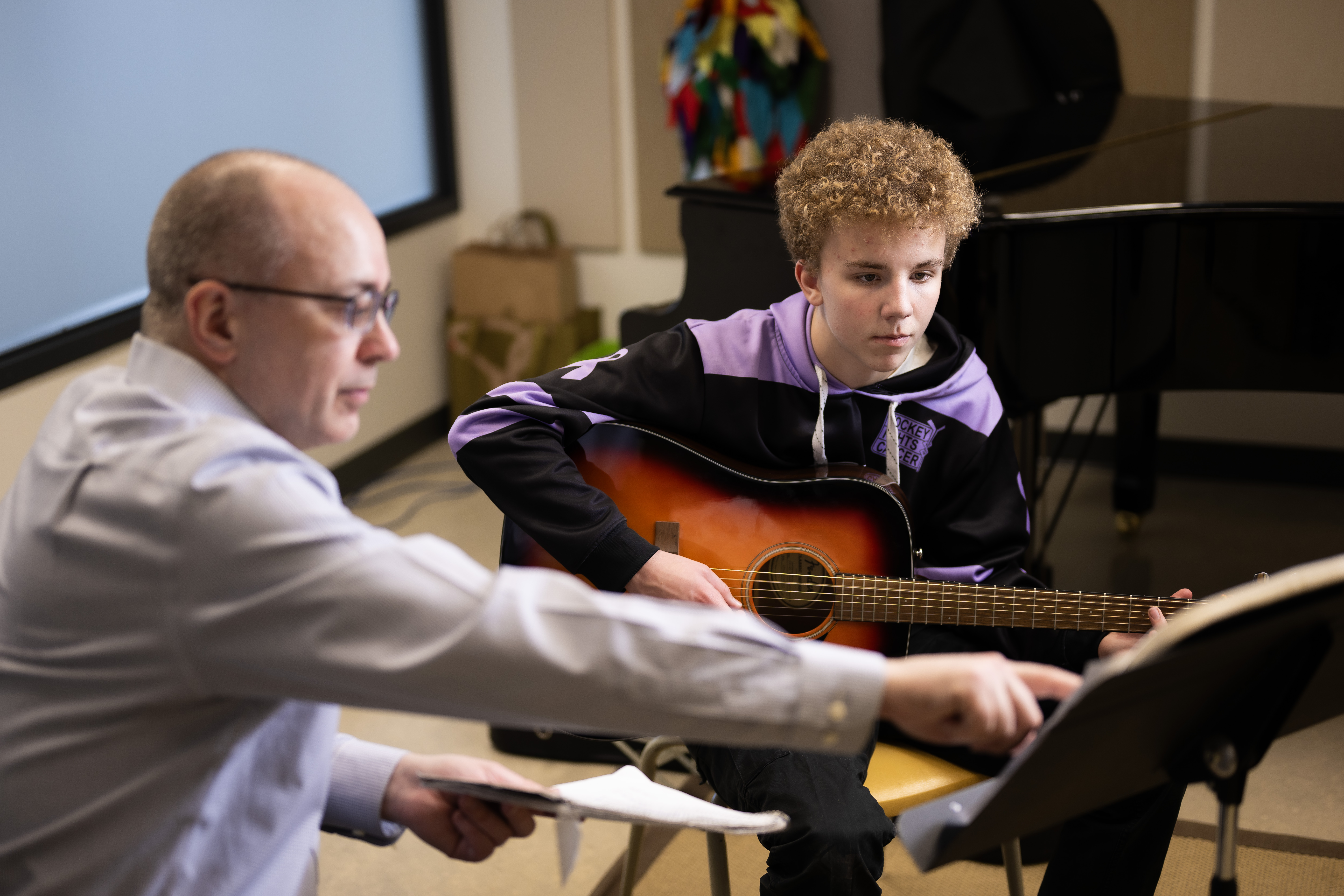 A student and teacher sitting and playing their guitars while looking at music.