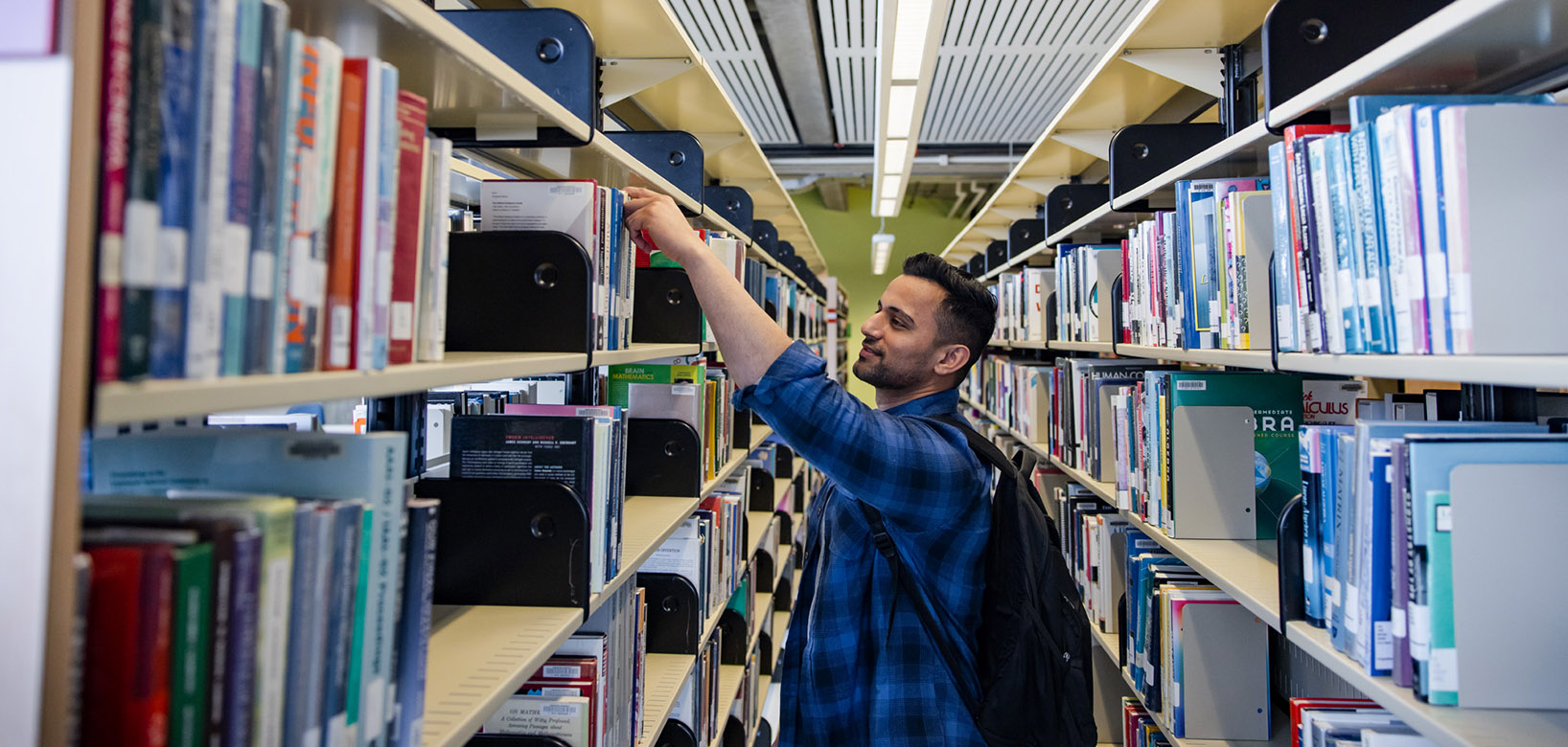A person selecting a book from a bookshelf in the Augustana Library.