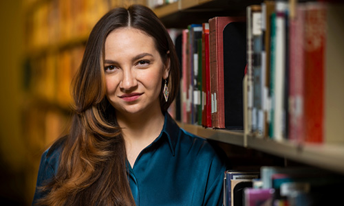 Photo of Willow White wearing a dark blue blouse and standing in front of rows of books.