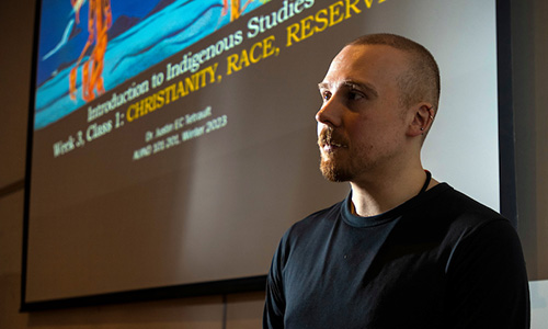 Side profile view of Justin Tetrault standing in front of a screen in a classroom.