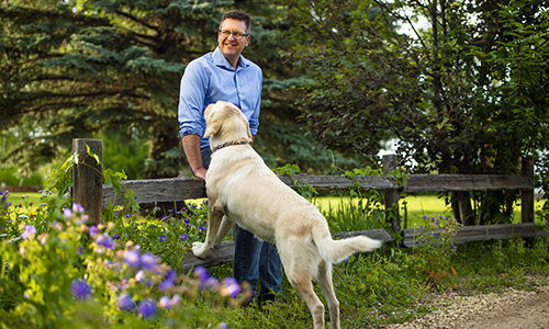 Clark leaning against a wooden fence post and a do leaning on the fence post beside him.