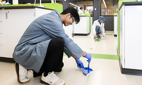 Students cleaning up fake glass in a campus lab.