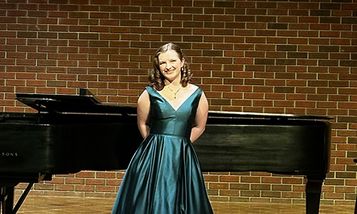 Emma Werbowesky in a formal green dress in front of a piano.