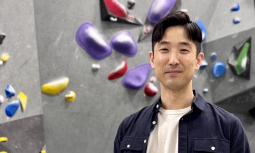 Kevin Yoon standing in front of a rock climbing wall.