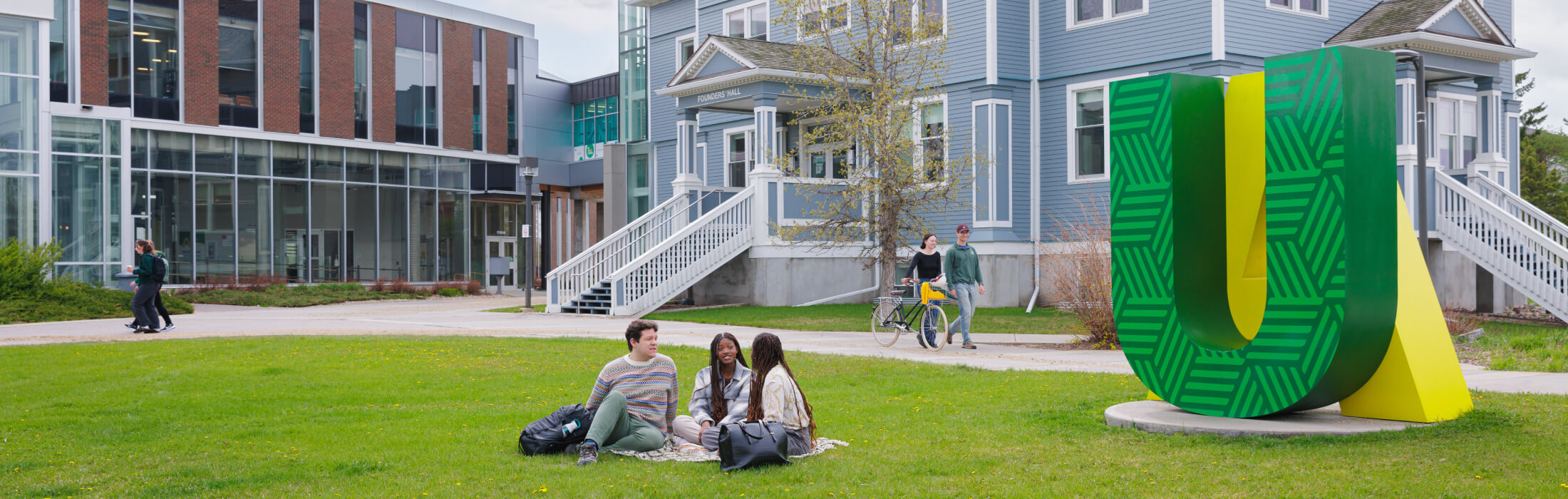Students on lawn with large green and gold 'U of A' sign at University of Alberta Augustana campus