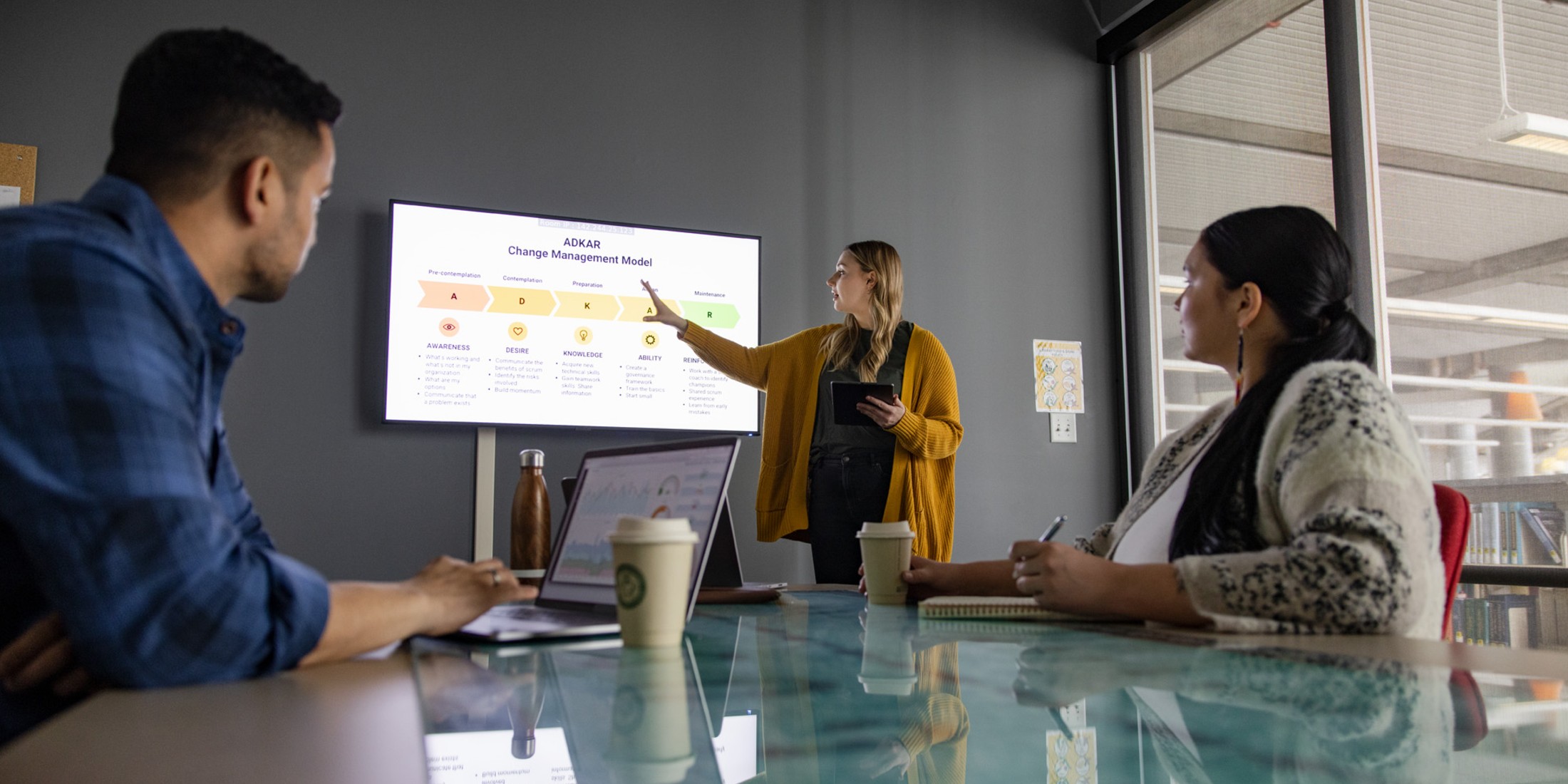 Three people in a meeting room looking at a screen