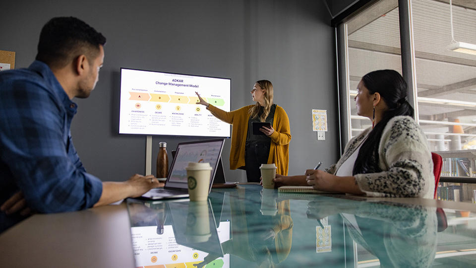 A person presenting a slideshow to two people sitting at a table in the Augustana library.
