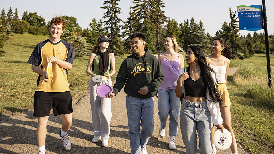 A group of people walking and conversing as they walk through Camrose's Jubliee Park in the summer.
