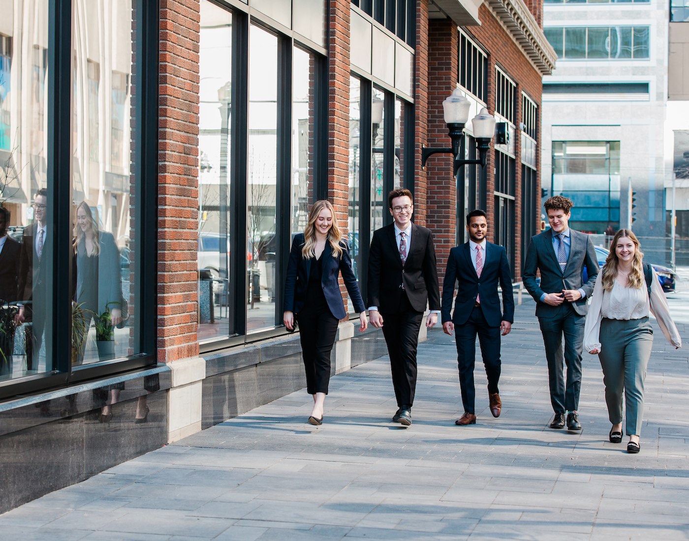 5 business students walking beside a brick building