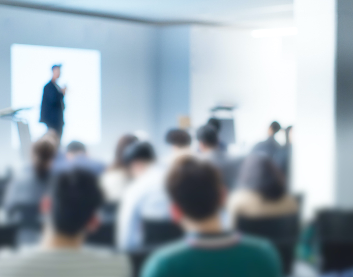 Blurry image of an instructor conducting a seminar in front of a podium