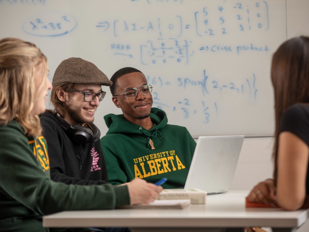 Four co-op students sitting at a table smiling and interacting with each other. 