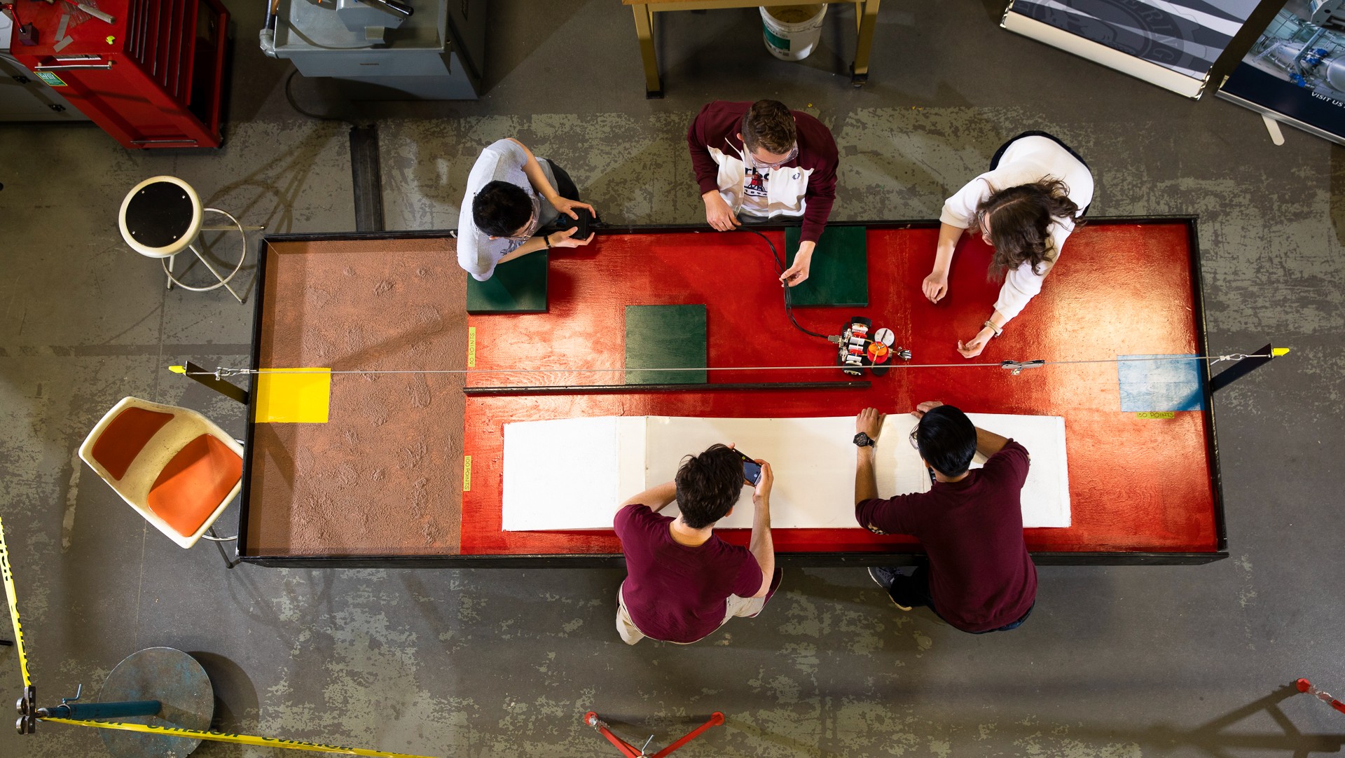 Five people working on an mechanical device image taking from top looking down.