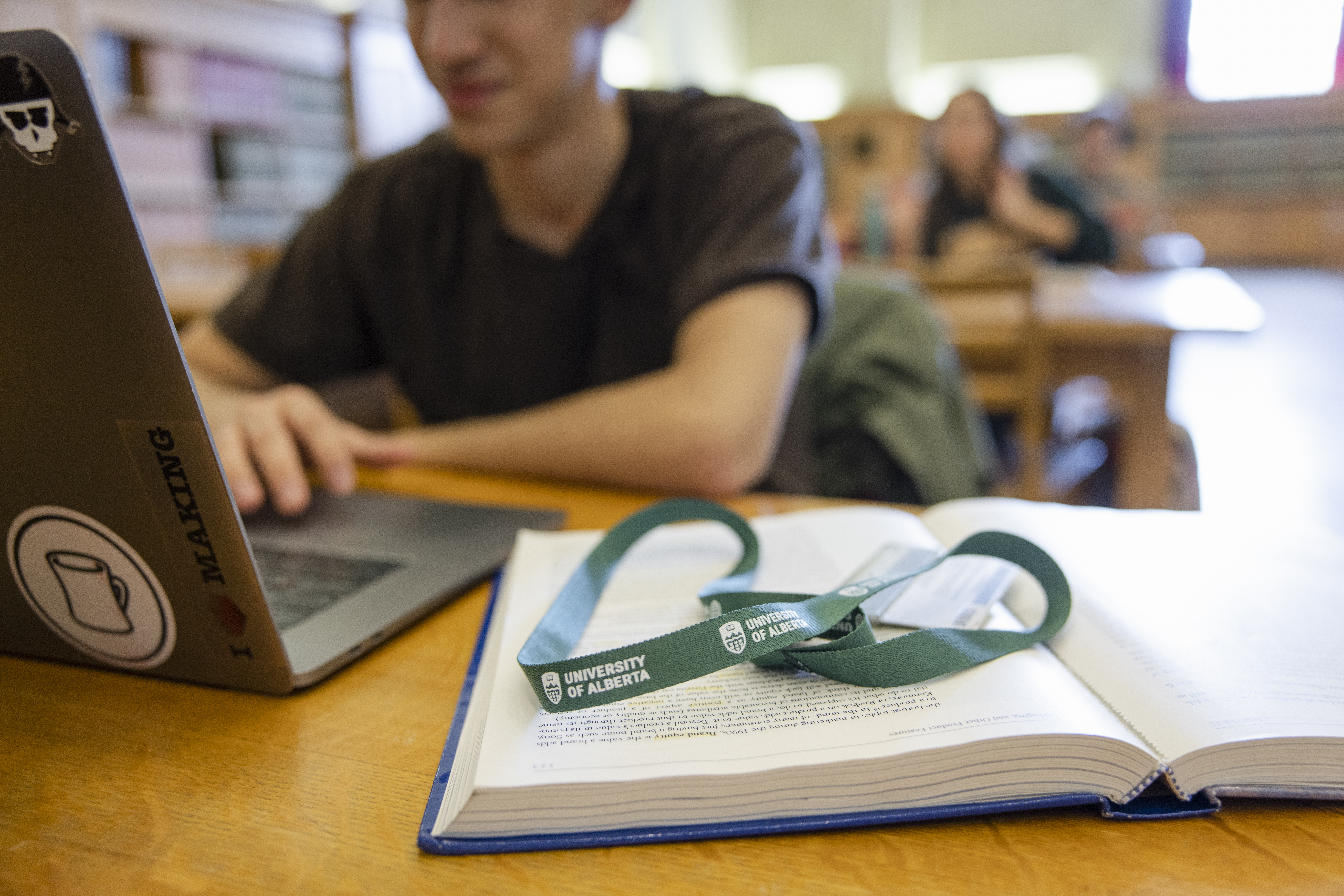 Book, open student reading, lanyard on book.