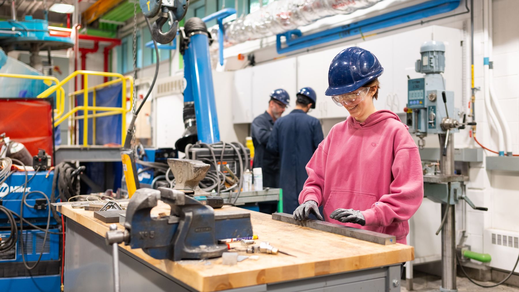 Woman in a hard hat at a wooden table surrounded by machinery