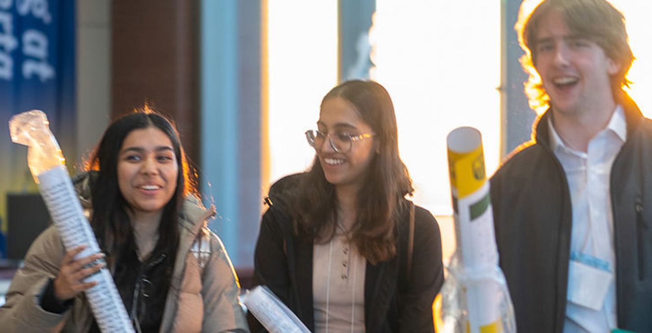 Undergraduate engineering students smile in an engineering building while holding their research posters.
