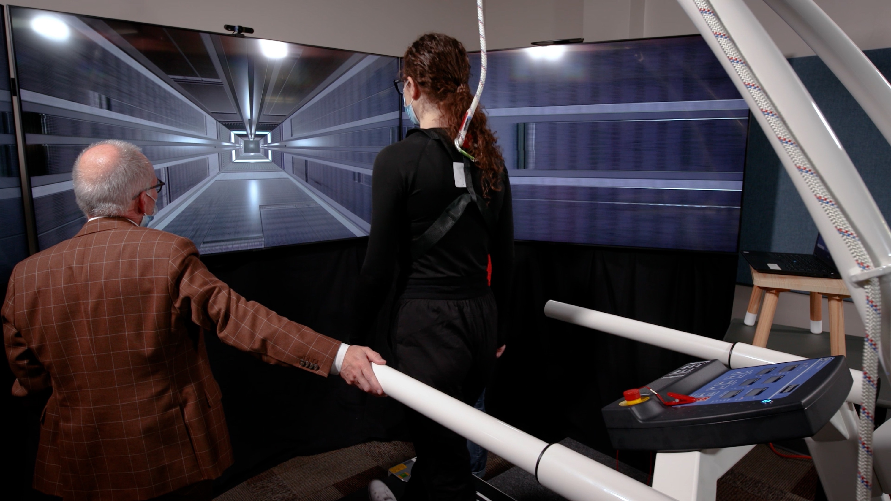 A woman walks on a treadmill towards a screen displaying an elevator shaft. (Photo: Geoff McMaster)