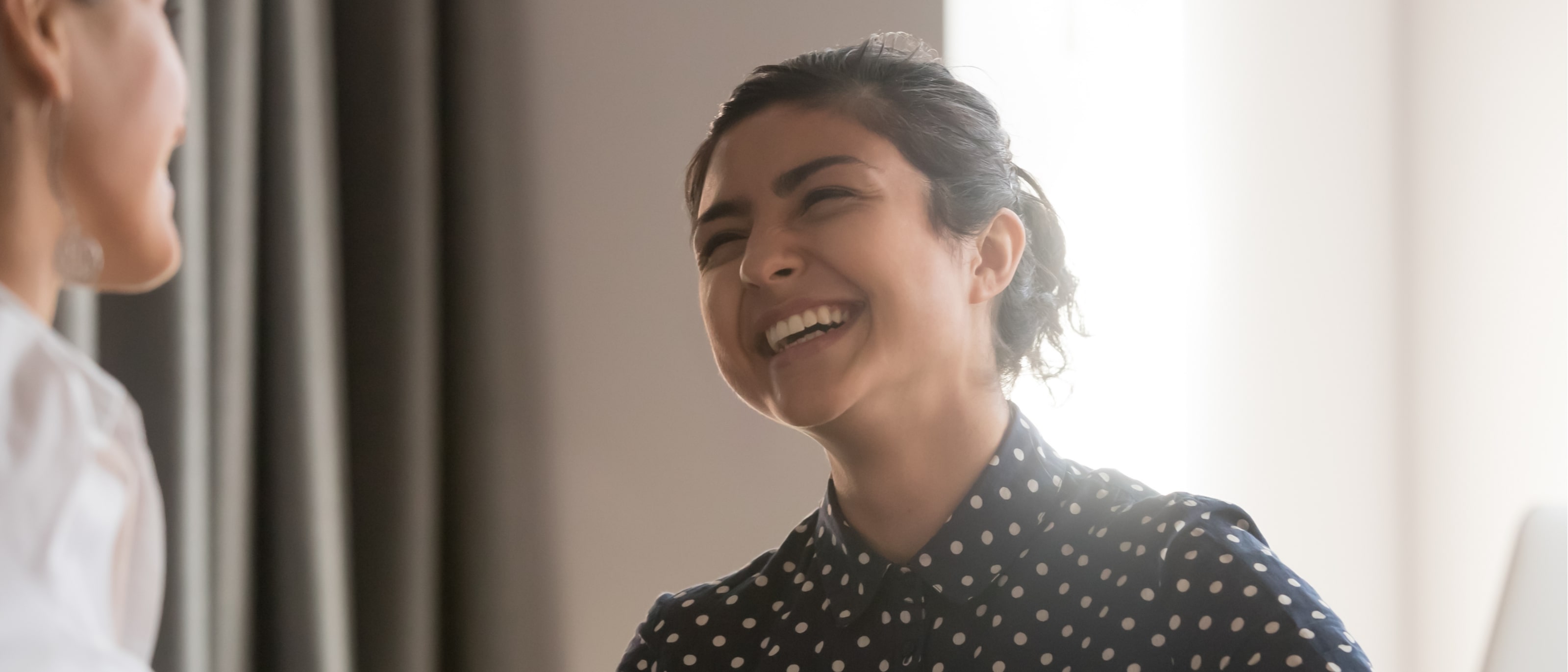 Happy cheerful young indian business woman enjoy chatting laughing with friendly female colleague at workplace, smiling hindu worker having fun talking working together with mate at break in office