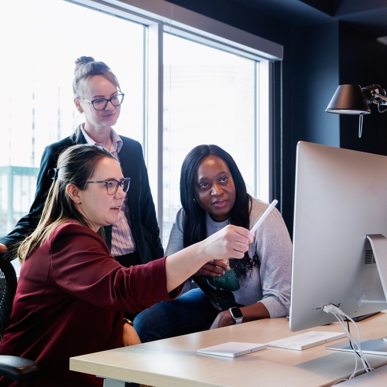 A woman pointing at a monitor while two other women watch