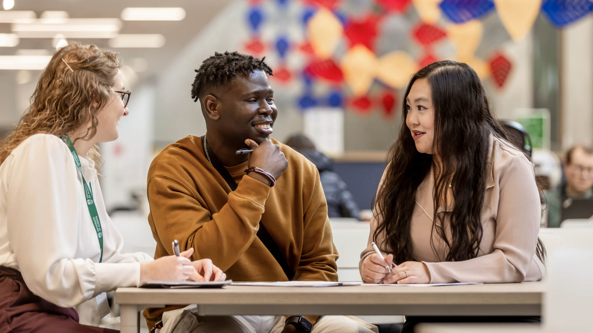 Students chatting around a table with pens and notebooks