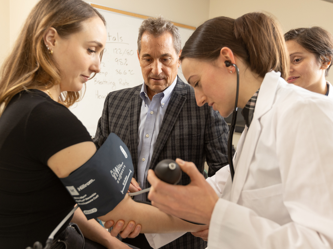 A medical student conducts a blood pressure reading on a patient under the eye of her preceptor.