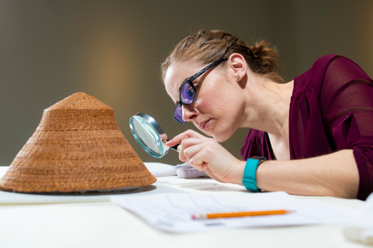 A woman examining a museum article with a magnifying glass