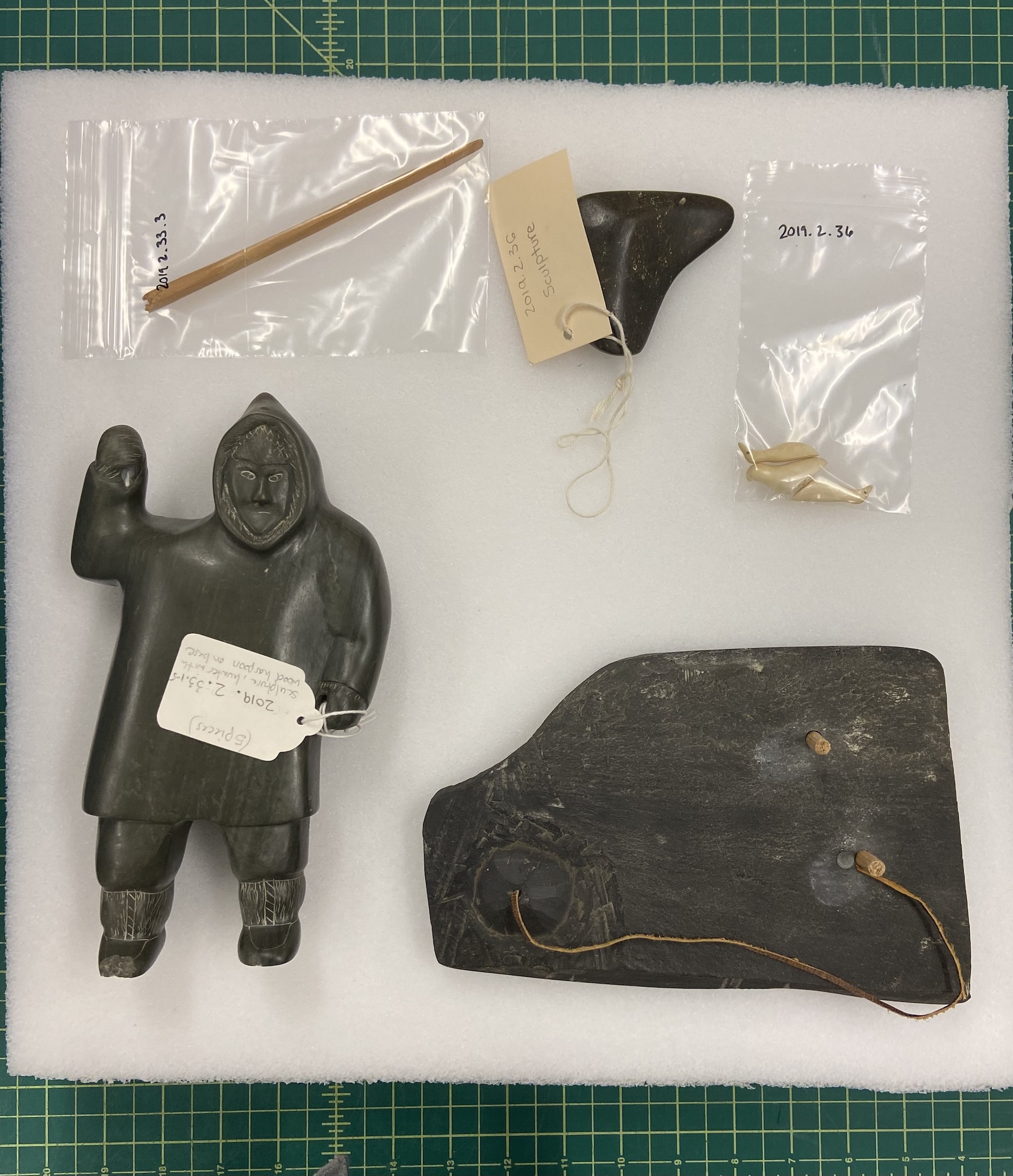 A grouping of stone and bone Inuit sculptures, including an Inuit hunter with his arm raised, rest on top of a block of white foam