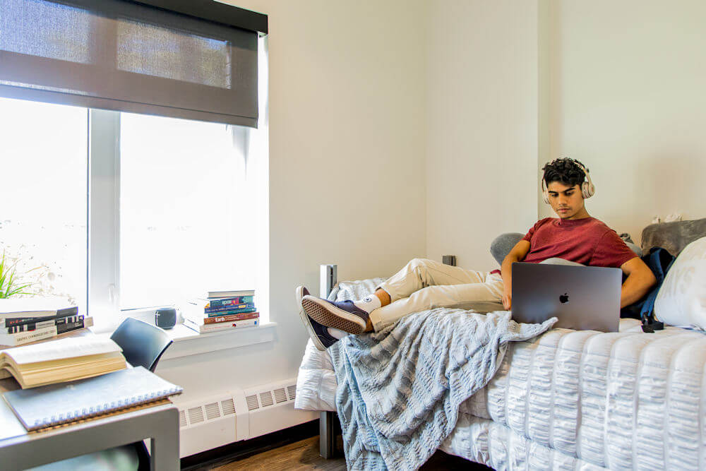 Student sitting on their bed with their laptop wearing headphones