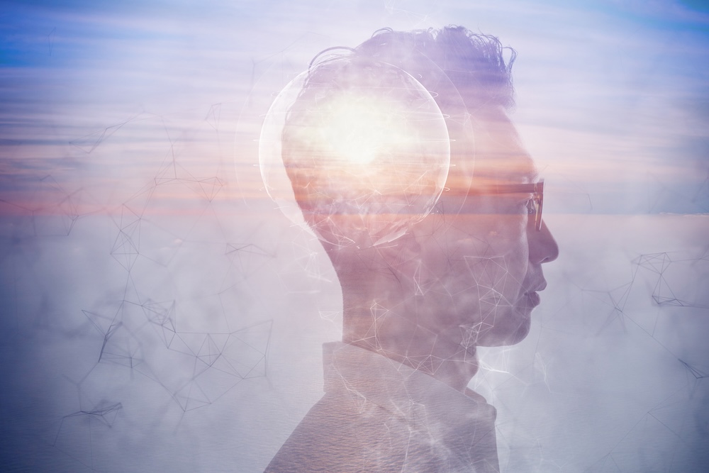 Surreal digital artwork depicting a profile view of a person’s face overlaid with an image of a human brain highlighted in bright light. The background features a blurred landscape and geometric shapes, creating a futuristic and abstract feel.