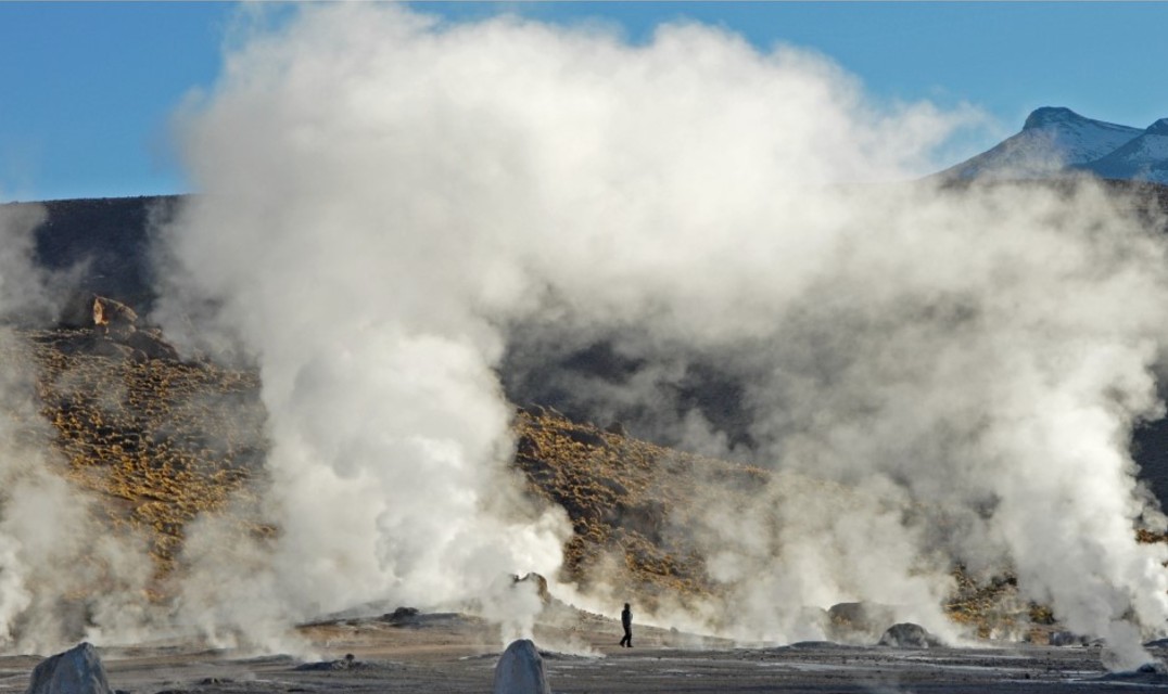 Clouds of steam billowing from geysers in front of a range of hills