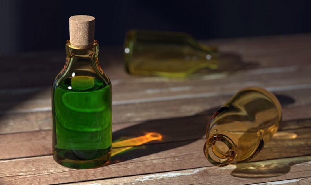 Corked bottle of green liquid standing on hardwood floor, two empty bottles lay next to it.