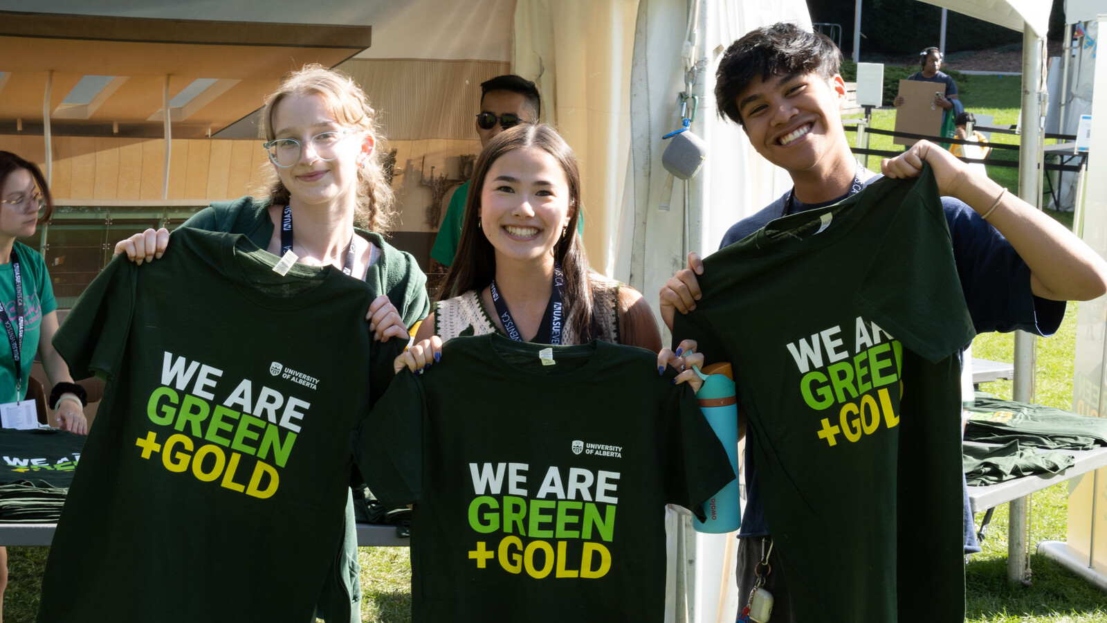 Three students pose with Green+Gold shirts at a U of A booth.