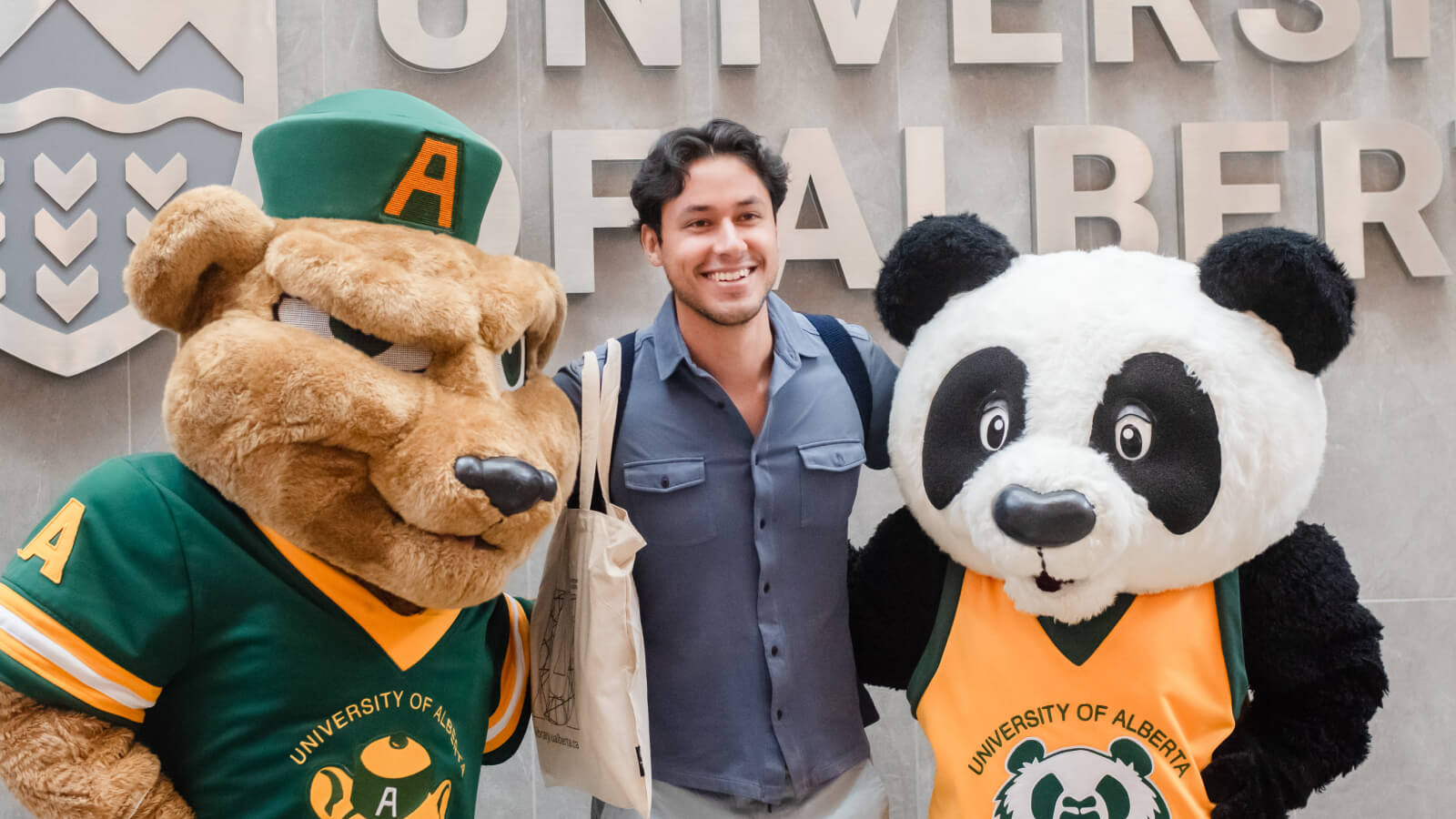 Student smiling and posing between Guba and Patches in fron of the campus sign.