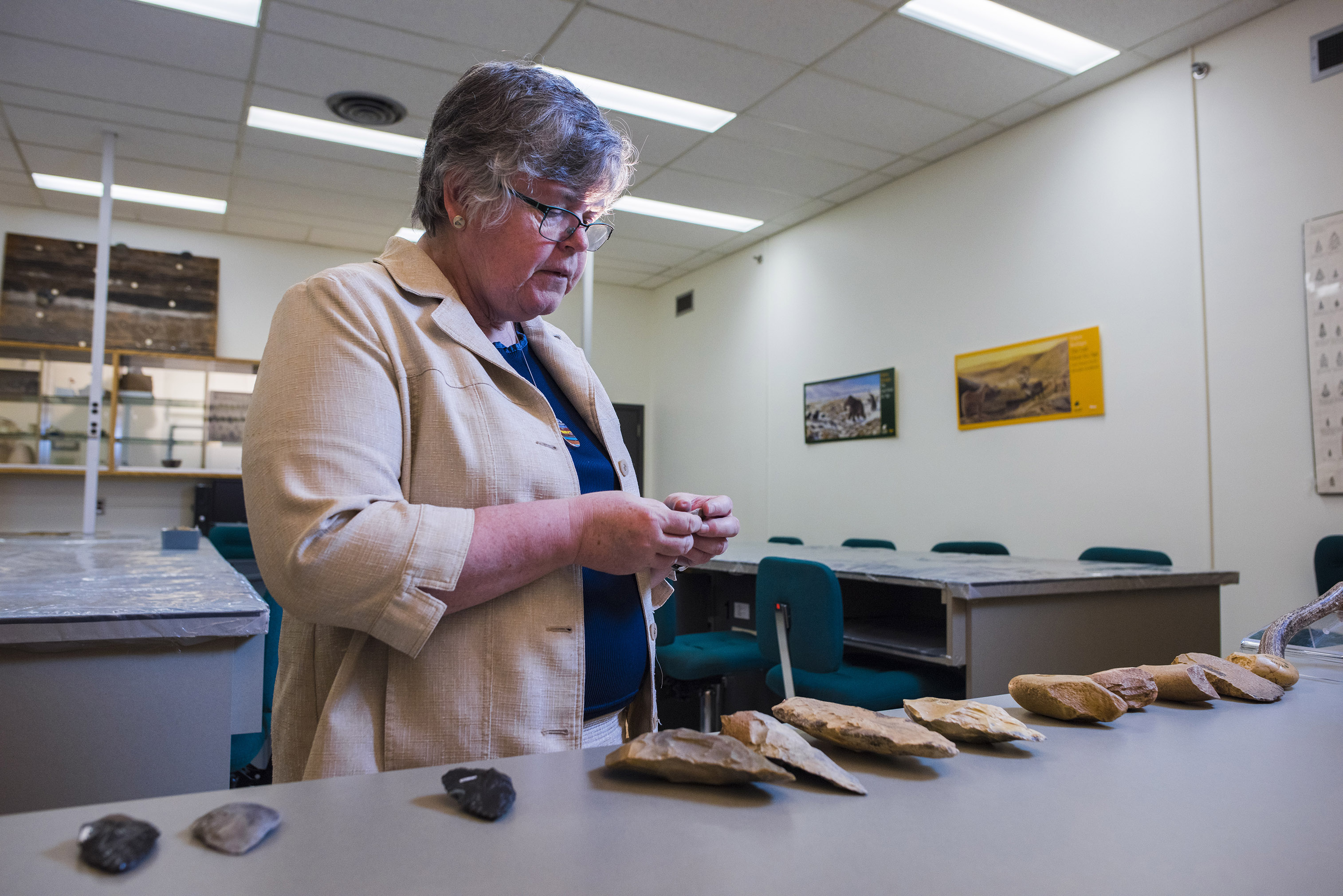 A woman stands by a table holding an artifact in her hands.