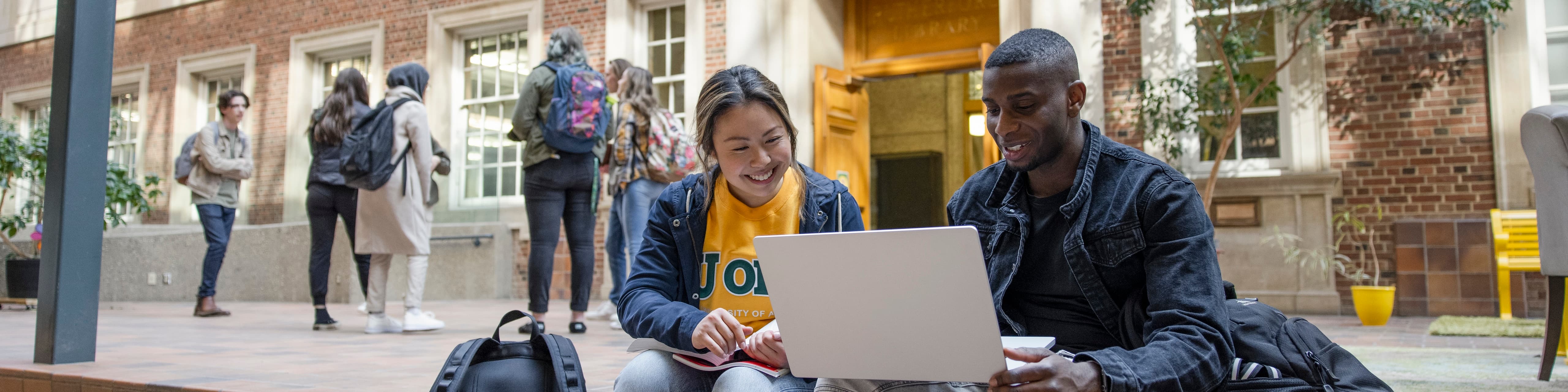Two students discussing classwork on a laptop